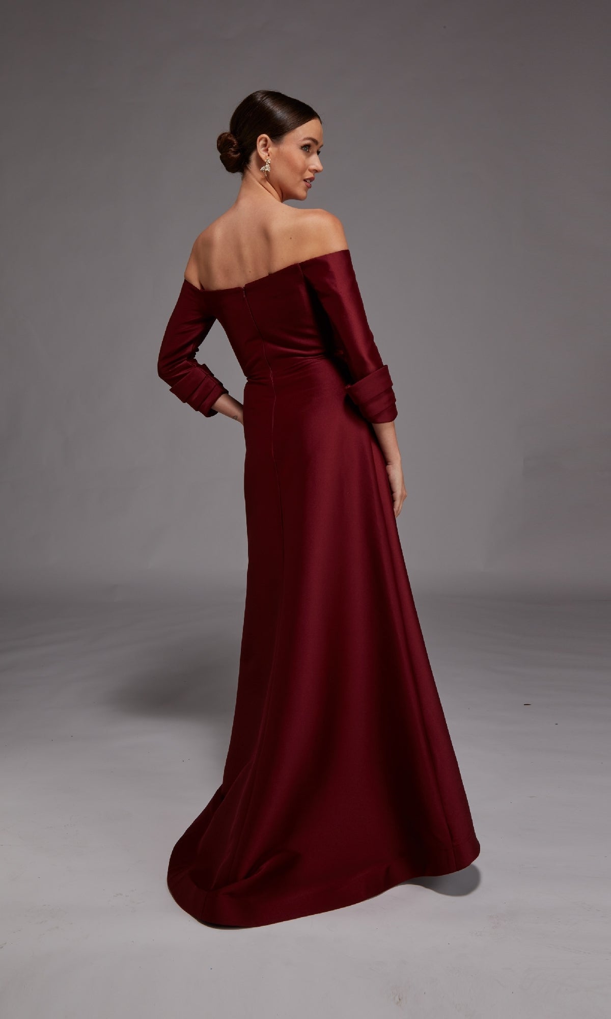 In a neutral studio, a woman in the Alyce 27859 long formal dress—floor-length, off-the-shoulder, and burgundy—stands with her back slightly turned; an elegant mother-of-the-bride option.